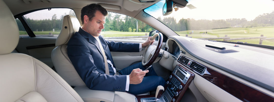 A stock photo of a man looking down at his phone while driving.