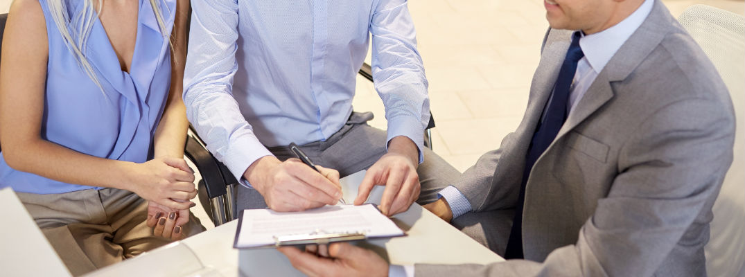 A stock photo of people signing paperwork at a dealership.