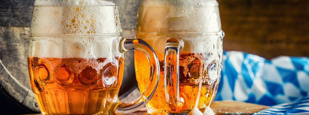 A stock photo of two full beer steins and an Oktoberfest tablecloth.