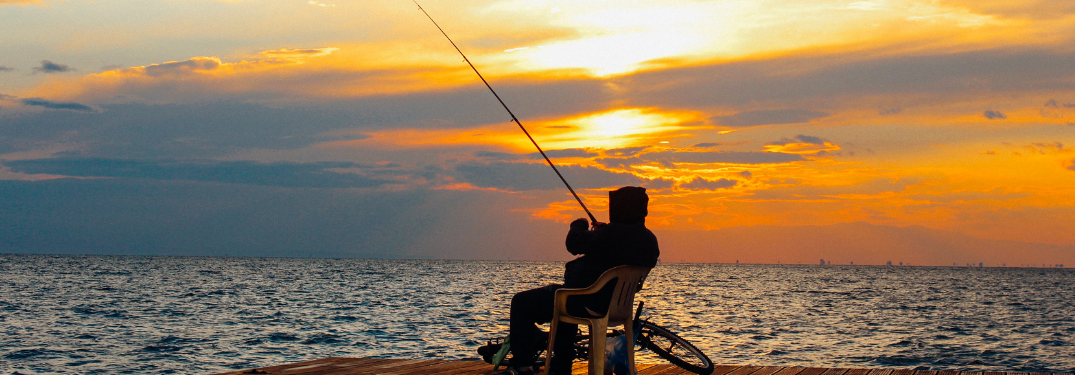 A man at a pier fishing at dawn