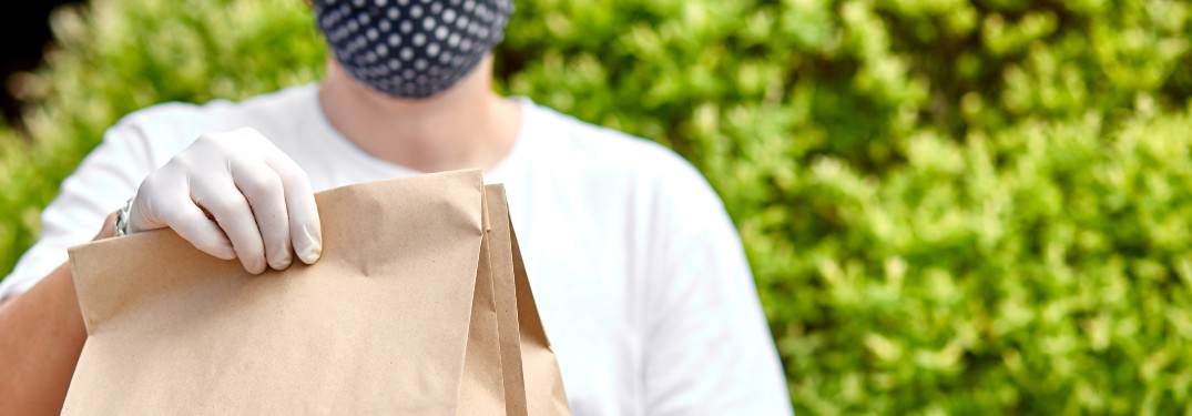 stock photo of man handing paper bags as delivery with mask and gloves