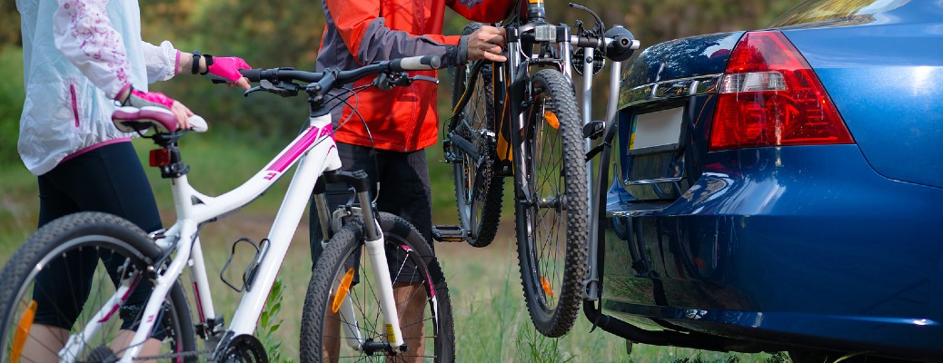 man and woman loading bikes onto trailer hitch bike rack on blue car