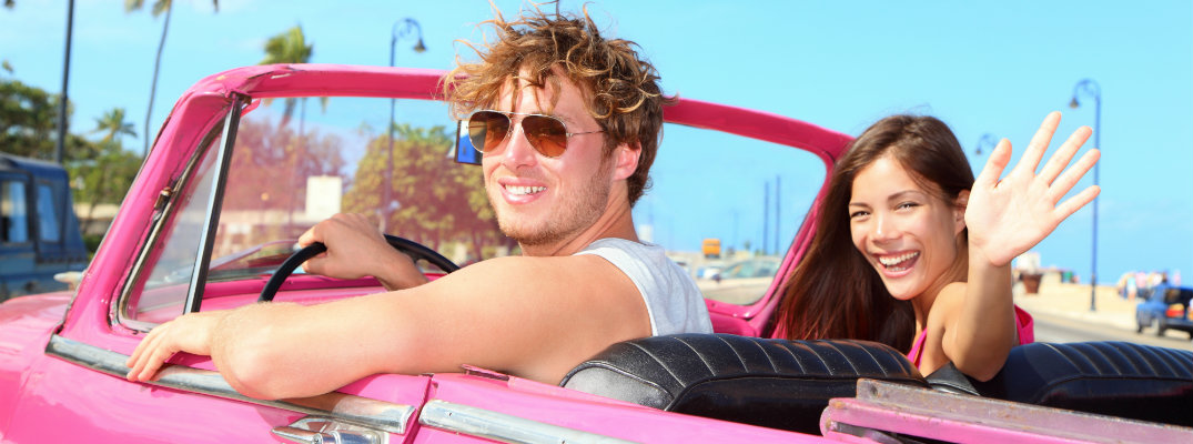 Man and woman facing camera and sitting in pink convertible