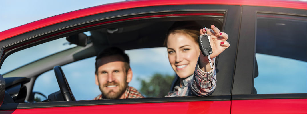 A stock photo of a young couple sitting in a car holding a set of keys.