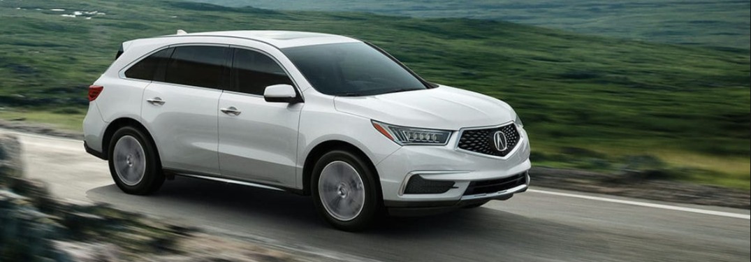 Front passenger angle of a white 2020 Acura MDX driving on a road