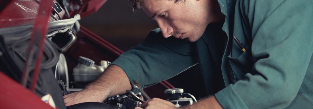 A mechanic fixing a car part under the hood.