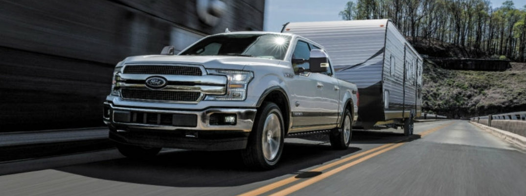 Silver 2018 Ford F-150 towing trailer on tree-lined country road