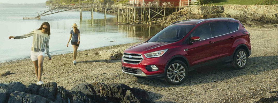 Two girls walking toward red 2018 Ford Escape on beach with water in background