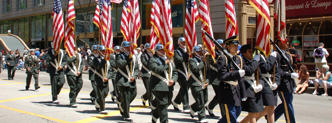 Uniformed military men and women holding American flags while marching in parade