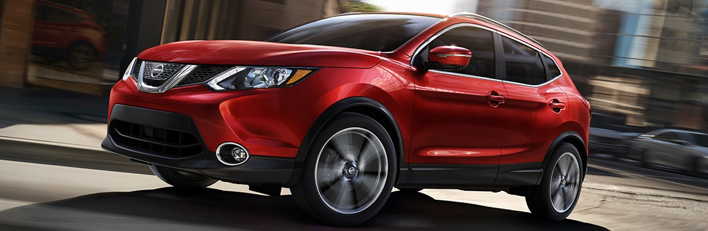 Exterior view of a red 2018 Nissan Rogue Sport driving down a city street