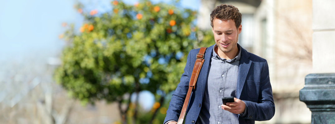 man walking to work in the sunny afternoon while looking at his smartphone
