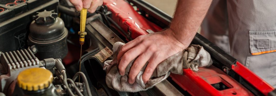 Hands of a mechanic checking for engine oil on a car in a garage