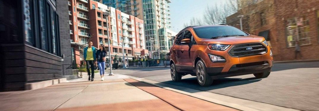 Side profile of the 2018 Ford EcoSport driving in a city next to people walking on a sidewalk