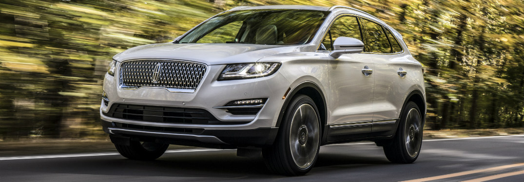 front and side view of white 2019 lincoln mkc driving through forest road