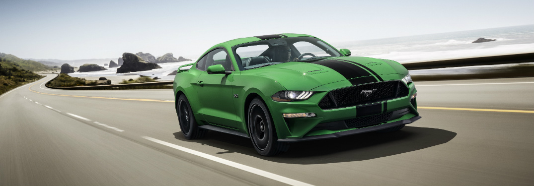green 2019 ford mustang driving on empty road near ocean