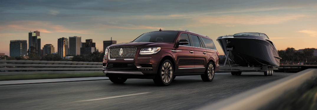 red 2018 lincoln navigator towing large boat on road