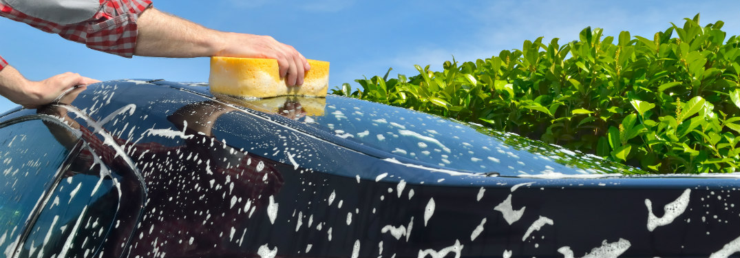 man wiping soap off exterior of car with yellow sponge outside