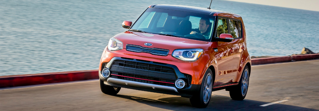 orange 2018 kia soul driving on road next to ocean