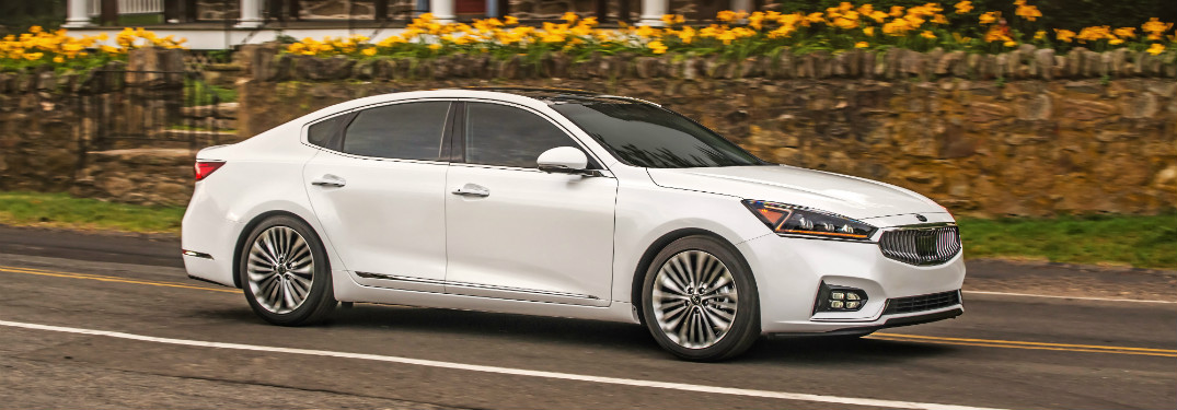 white 2018 kia cadenza driving on road in front of brick house