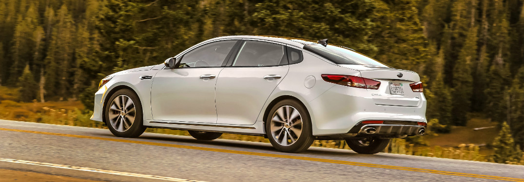 side view of white 2018 kia optima driving on forest road