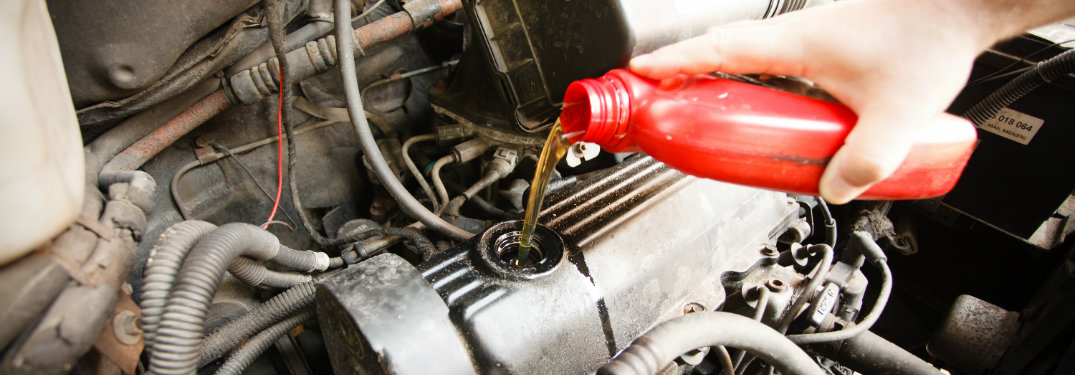 person pouring oil into an engine from a red plastic oil container