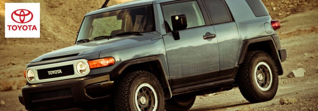 A green 2014 Toyota FJ Cruiser drives along rugged earth with a Toyota logo in the upper lefthand corner.