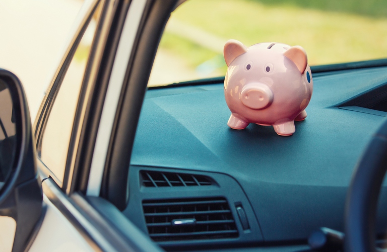 A piggy bank sits perched on the dash console of a car
