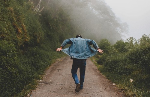 man walking on foggy trail flipping up ends of jean jacket