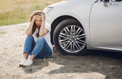 worried young woman sitting on ground next to broken down car