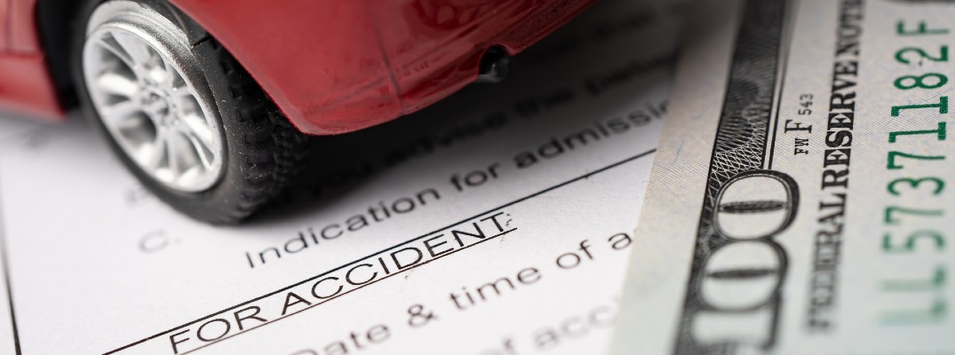 A stock photo showing a $100-dollar bill and toy car sitting on an insurance form.