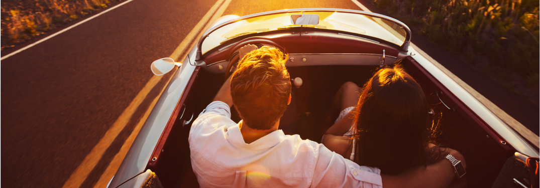 bird's eye view of couple driving in convertible at sunset