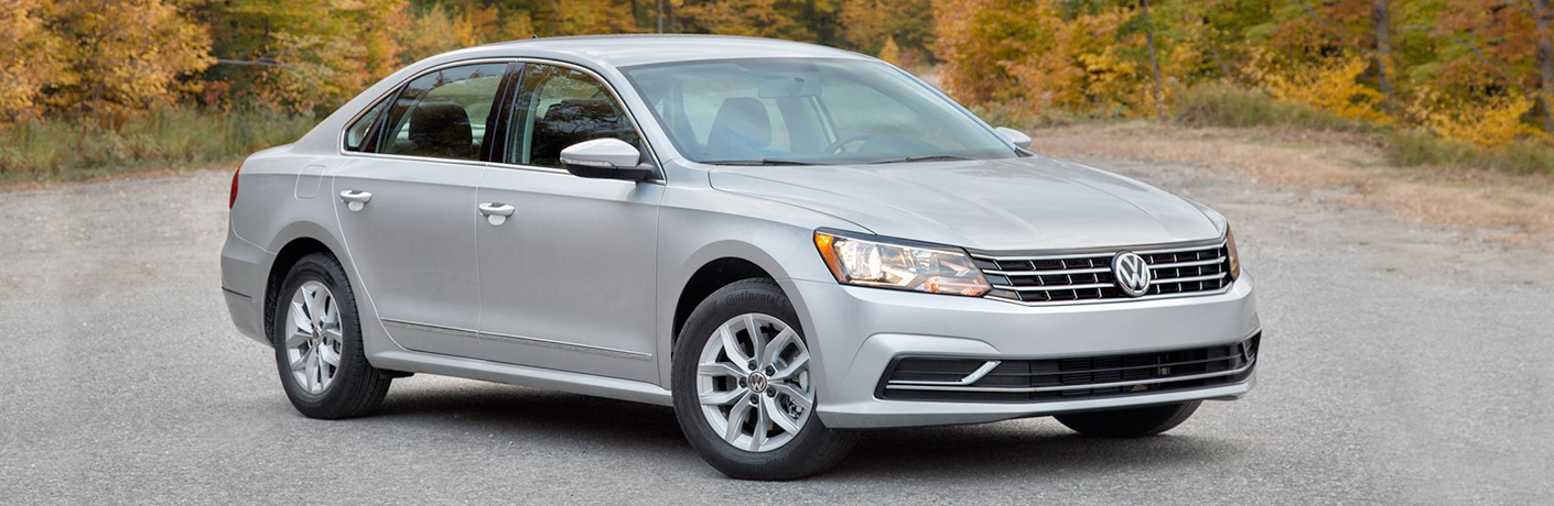 A grey 2018 Volkswagen Passat parked in the road with trees behind it.