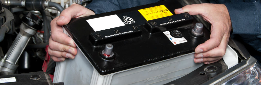 man pulling car battery out of vehicle