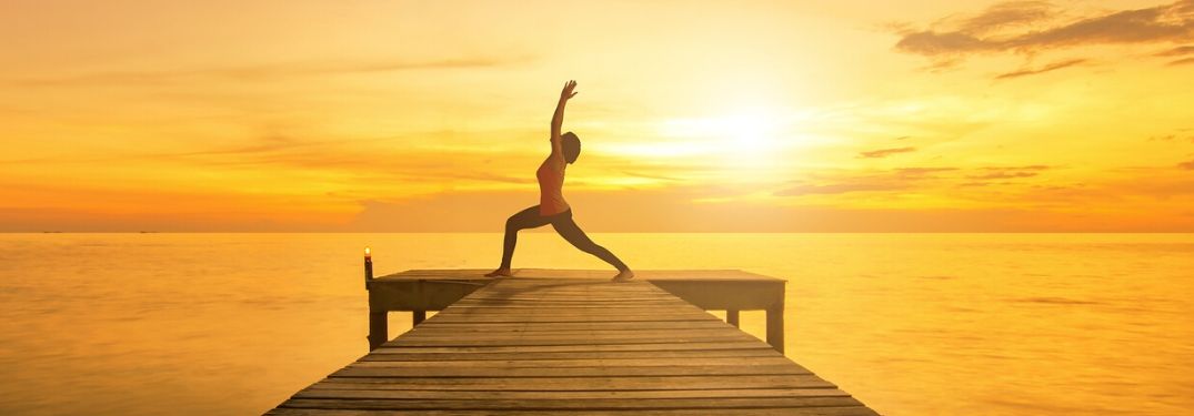 person doing yoga at end of dock during sunset