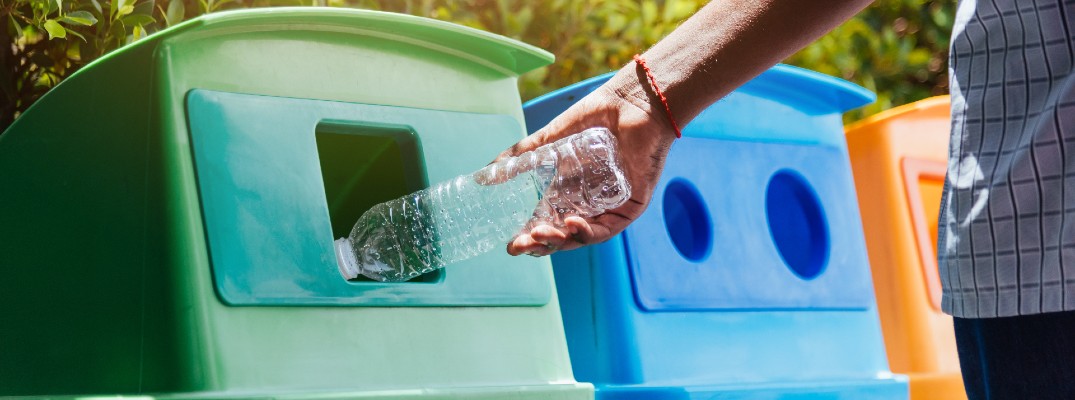 A person placing a plastic bottle in a recycling bin.
