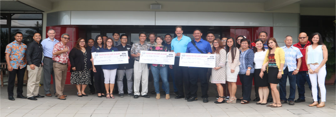 people standing in front of dealership with big checks
