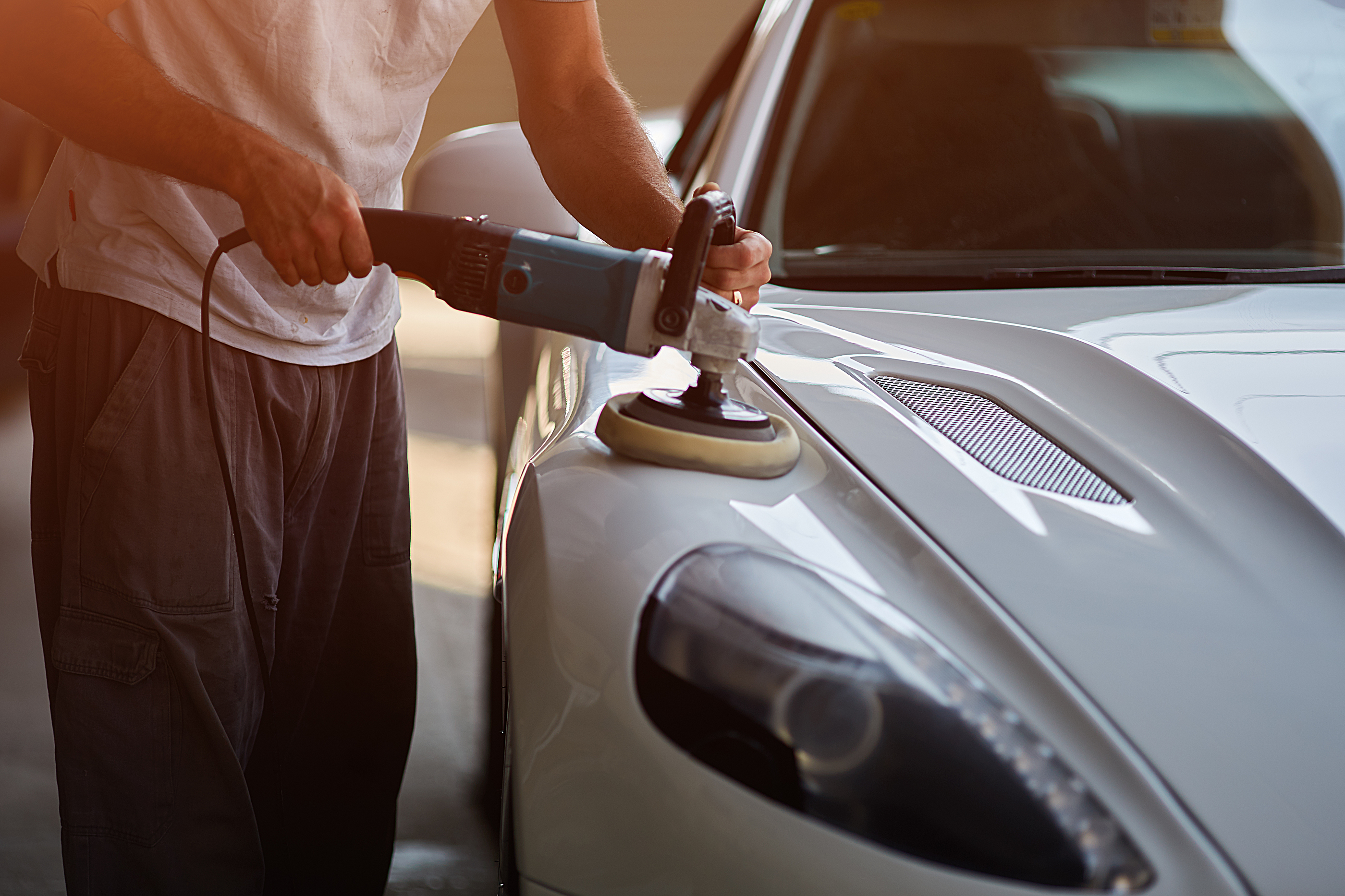 person buffing a white car luxury pants shirt windshield headlight front end hood ornament notebook plug extension cord service bay