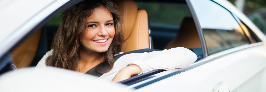 woman in driver seat of car looking out window and smiling
