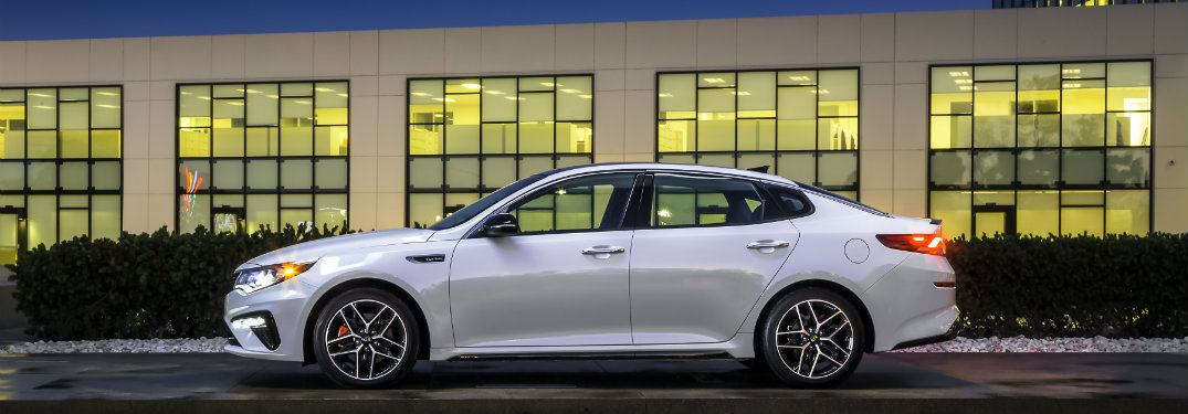 left side view of white kia optima driving by building
