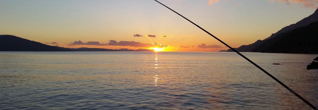 Someone fishing in a large lake at sunset