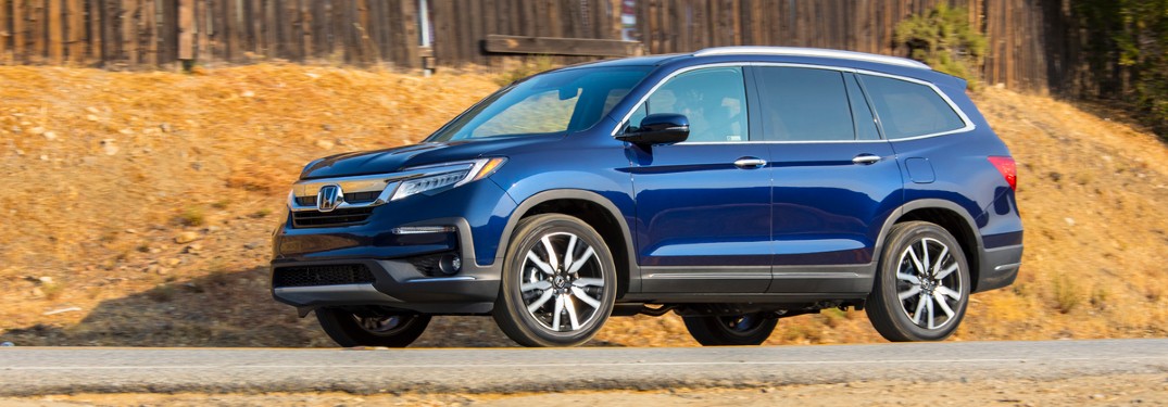 2021 Honda Pilot Elite 2019 shown blue parked in front of hill with wood fence