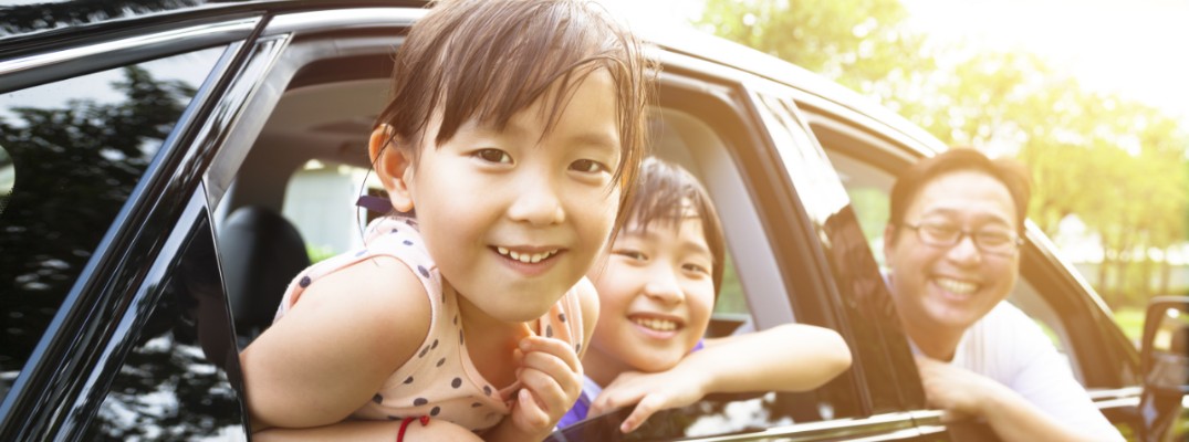 A little girl and her family sitting inside a car and smiling