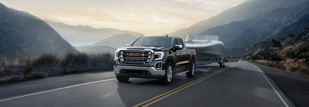 2019 GMC Sierra hauling a boat on a mountain road at sunrise