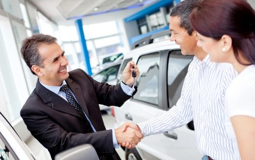 Salesperson holding keys shaking hands with a man and woman