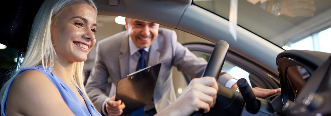 Woman behind the wheel of a car, looking at the dashboard with a sales person looking on