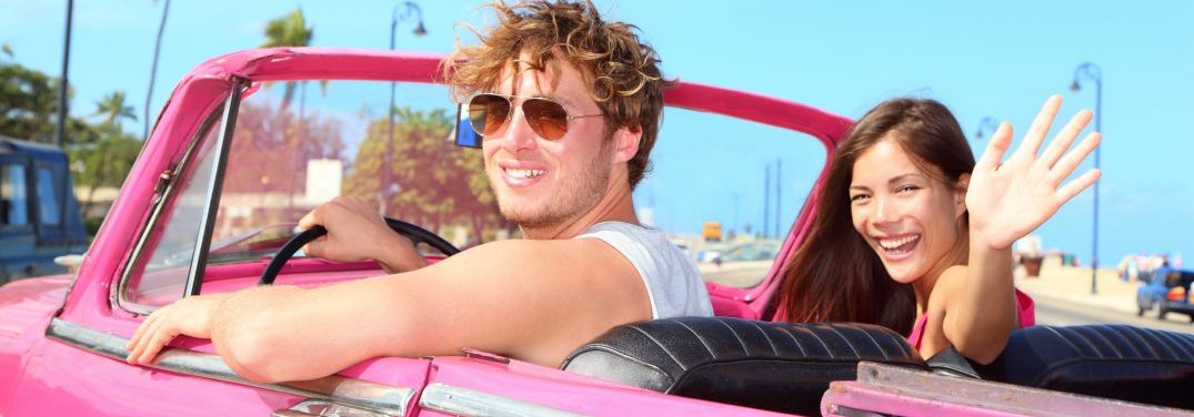 Two young people driving in a hot pink vintage convertible on a sunny day