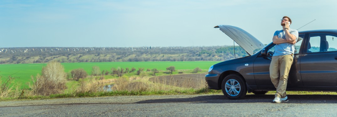 Man calling for help next to his car with the hood open and an open field in the background