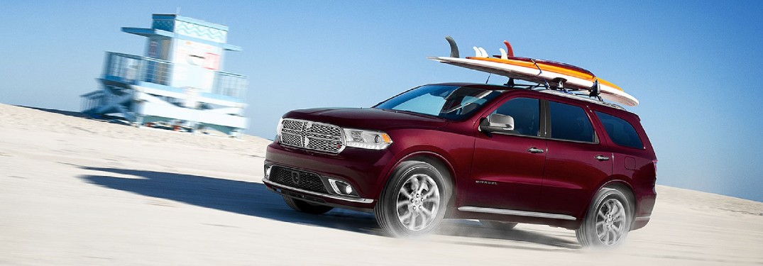 Front driver angle of a red 2020 Dodge Durango with surfboards mounted on its roof rails and driving on a beach