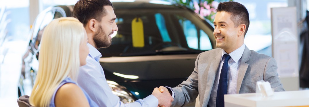 Happy couple shaking hands with a car salesman