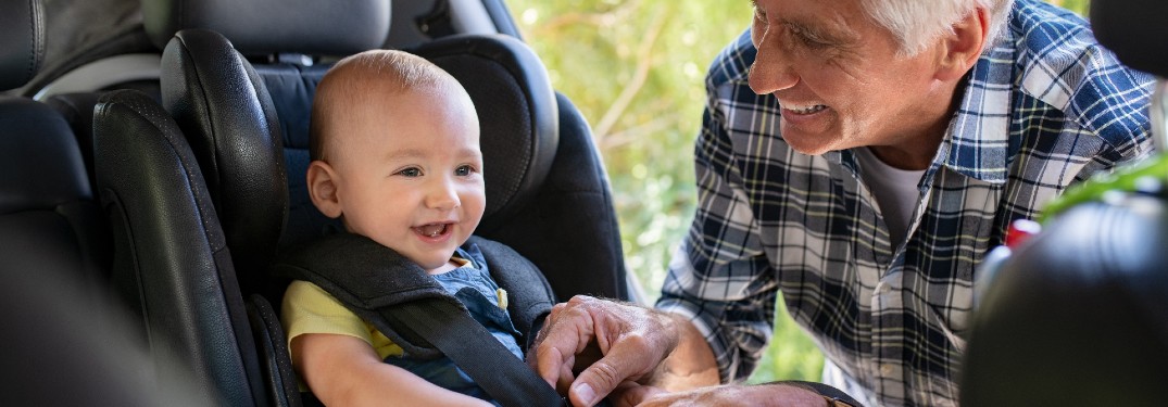 Grandfather buckling a baby boy into a car seat